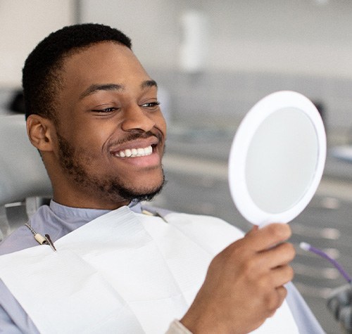 Man smiling while looking at reflection in handheld mirror