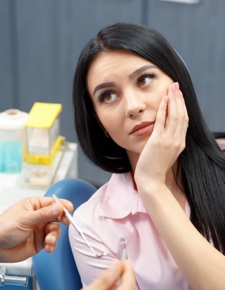 Woman in dental chair holding her cheek in pain
