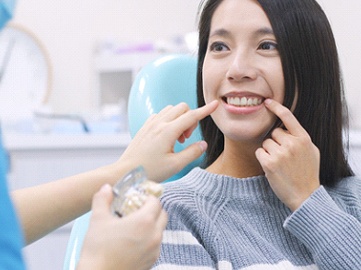 Woman in dental chair pointing to her smile.