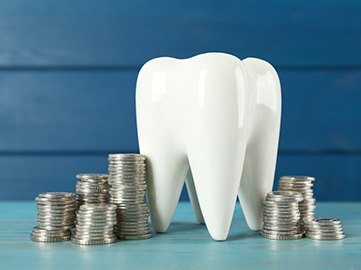 A large tooth model surrounded by silver coins
