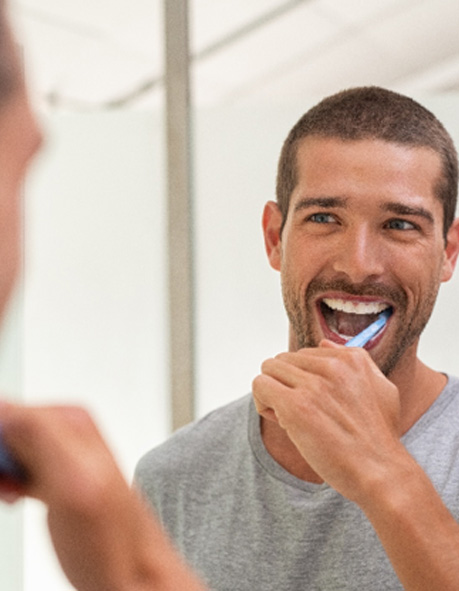 Man smiling while brushing his teeth in bathroom