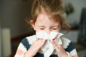 child with a cold blowing her nose