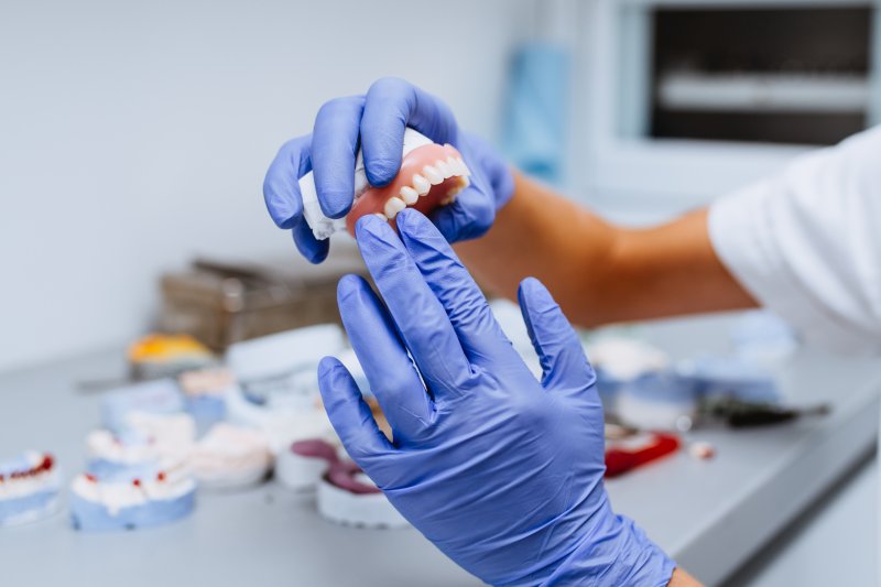  denture being assessed by a dentist wearing purple gloves
